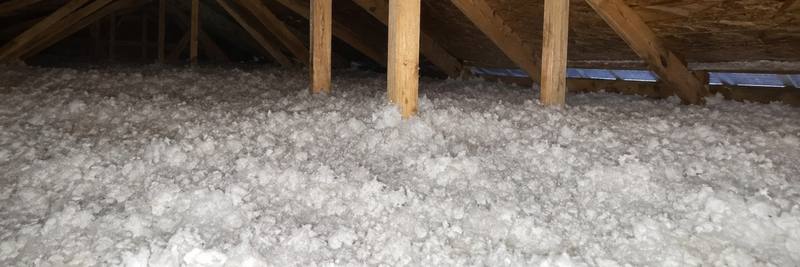 Wide attic with deep white blown-in fiberglass insulation spread evenly under the roof trusses