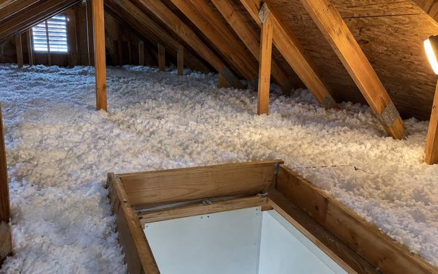 Attic hatch opening framed by a raised wooden dam in deep white loose-fill insulation