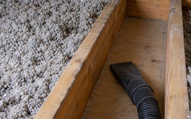 Vacuum hose nozzle lifting old cellulose insulation out of a joist bay