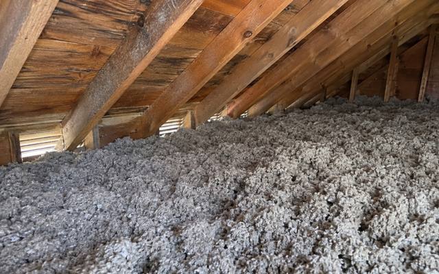 Deep grey blown-in insulation reaching the rafters along the eaves of an attic