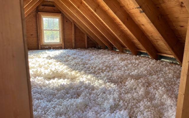 Thick white blown-in fiberglass across an attic, lit by a gable window
