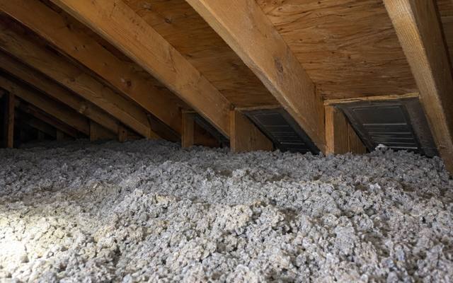 Grey blown cellulose spread across an attic floor, with light coming through the soffit vents