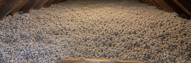 Even layer of grey loose-fill cellulose covering an attic floor beside the open hatch frame